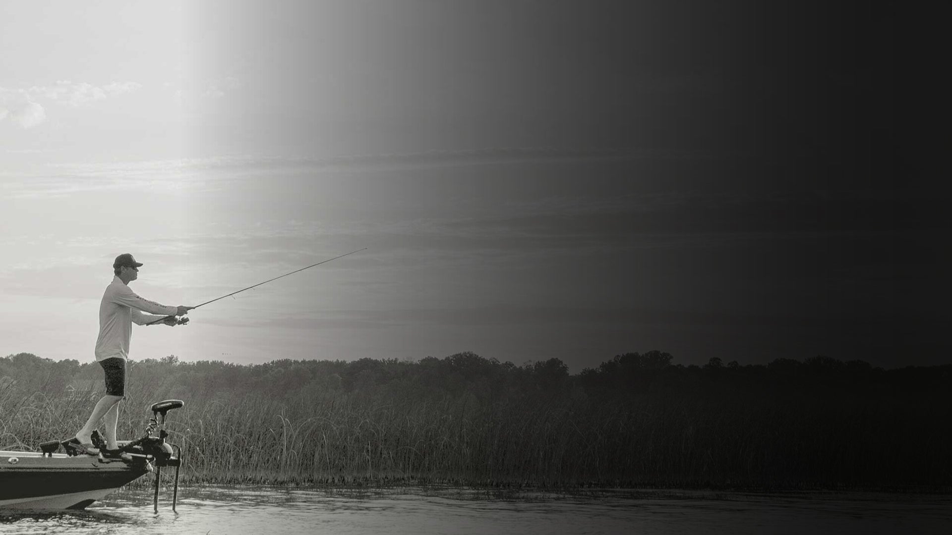 Person fishing from a boat on a lake with trees in the background